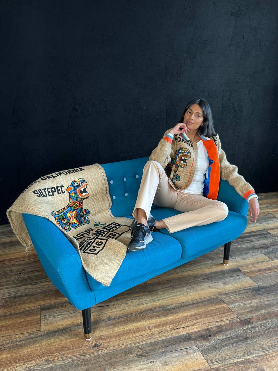 Young lady sitting on a blue sofa and wearíng a spectacular eco-jacket handcrafted from used rare Mexican coffee sacks